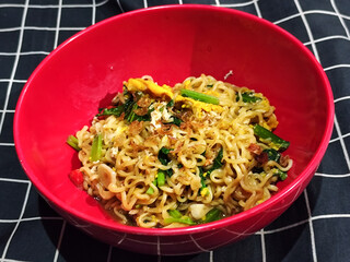 A bright red bowl filled with delicious fried noodles with sliced ​​egg, mustard greens, crispy...