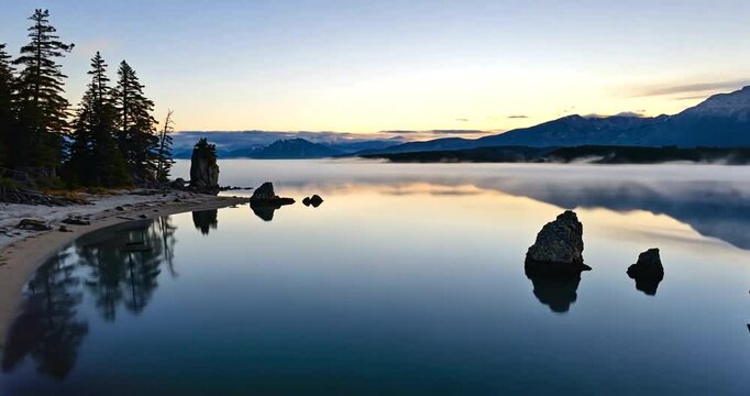 Serene lakeside view at dawn with mist rising over water and mountains in the background