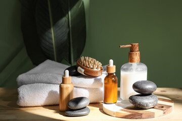 Bottles of cosmetic products, spa stones and bath supplies on wooden table near green wall