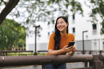 Smiling young woman using smartphone leaning on railing in a park