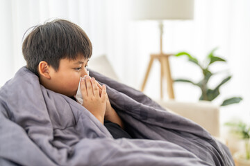 Young asian boy sneezing or blowing his nose and mouth with tissue, cold allergies or illness,...