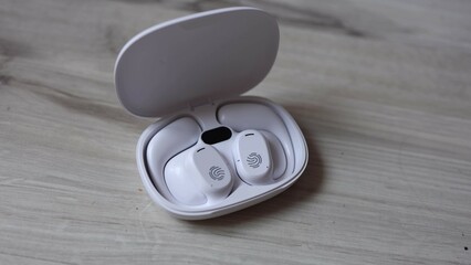 Closeup of white wireless earbuds with fingerprint touch control resting inside an open charging...