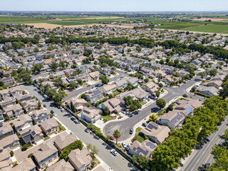 Aerial view of suburban residential neighborhood with houses and streets, lush green trees and open fields in background, community planning real estate development concept