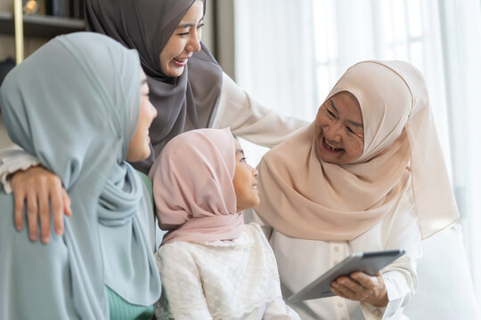 Muslim family four generations sitting on sofa enjoying tablet, joyful moment with grandmother, mother, daughter and aunt, digital sharing, love, connection, home happiness family lifestyle