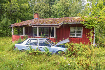 Abandoned house with a car wreck in a overgrown garden