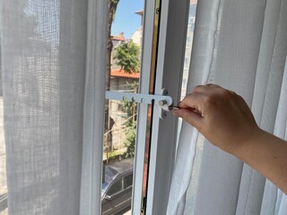 Child safety window lock installed on a modern plastic window. A person is adjusting the lock to...