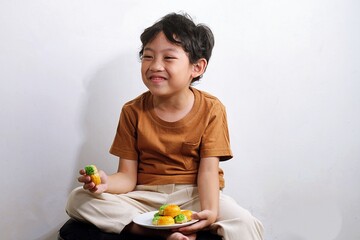 Happy Asian boy eats traditional nastar pineapple tart at home. A candid and joyful moment of childhood with local Indonesian snack.