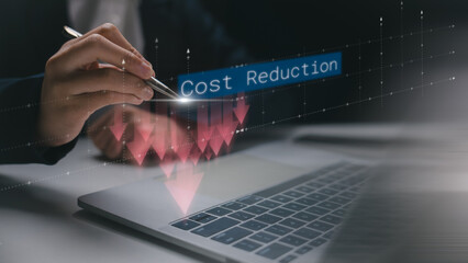Businessman's hand using a pen with cost reduction graph overlay on a laptop. Concept of minimizing business expenses, financial control, and smart budgeting strategies.