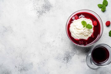 Delicious dessert with red jelly, cream, and fresh raspberries served in a bowl alongside a glass of dark beverage on a textured background, perfect for culinary imagery