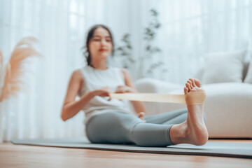 Young Asian woman doing pilates workout using elastic strap pulling with arms for shoulder training...