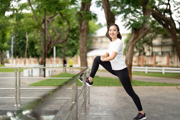 Dynamic Fitness Pose. Young woman stretching leg on railing in park, smiling confidently.