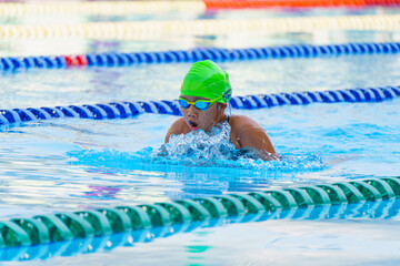 Swimmer child swims breaststroke swimming style in a race swimming pool. Water sports and...