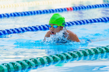 Swimmer child swims breaststroke swimming style in a race swimming pool. Water sports and...