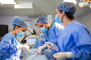 Surgeons performing an operation in a sterile surgical room. Focused medical team wearing scrubs, masks, and gloves while conducting a procedure under bright surgical lights.