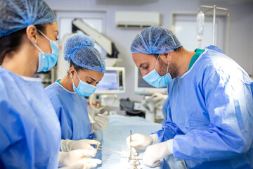Surgical team performing an operation. Three medical professionals in sterile clothing are focused...