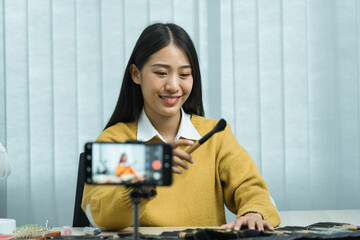 Young asian woman vlogging about cosmetics skin care items products on table with her video camera and demonstrates product use and reviews for her online blog channel.