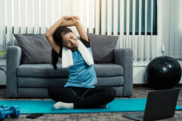 Asian woman stretching during a yoga class with a trainer at her laptop computer at home.