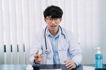 Asian doctor wearing glasses and white uniforms with a stethoscope provides online counseling to patients during the virus outbreak keeping a social distance.
