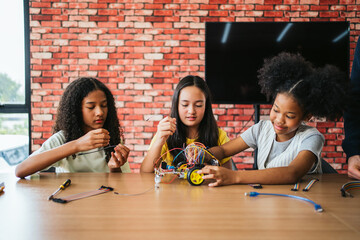 Three diverse schoolgirls building a robotic car with wires in a classroom. Engaging in STEM learning, teamwork, and coding activities. Hands-on education encourages creativity and innovation.