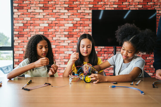 Three diverse schoolgirls building a robotic car with wires in a classroom. Engaging in STEM learning, teamwork, and coding activities. Hands-on education encourages creativity and innovation.