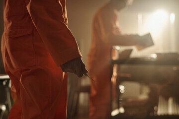 Man holding sharp metal object in hand standing in foreground while another man reading book at cart in prison library setting with sunlight streaming in