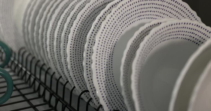 Clean white plates with delicate patterns are neatly arranged on a dish rack in a warm kitchen setting. This showcases an organized space after meal preparation, highlighting kitchen cleanliness.