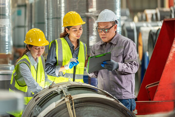 Construction workers inspecting blueprints and discussing project plans at an industrial site with safety gear including helmets and reflective vests in a modern manufactu setting