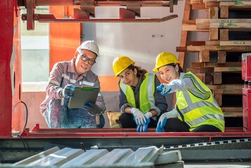 Three industrial workers in safety gear inspecting a metal sheet in a woodworking shop with stacks of wood in the background du daytime
