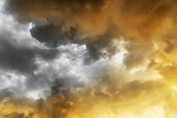 Dramatic cloudy sky with dark storm clouds and bright golden sunlight breaking through creating a...