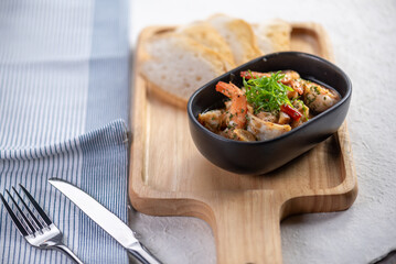 A bowl of sauteed shrimp with garlic and herbs, served with toasted bread on a wooden board.