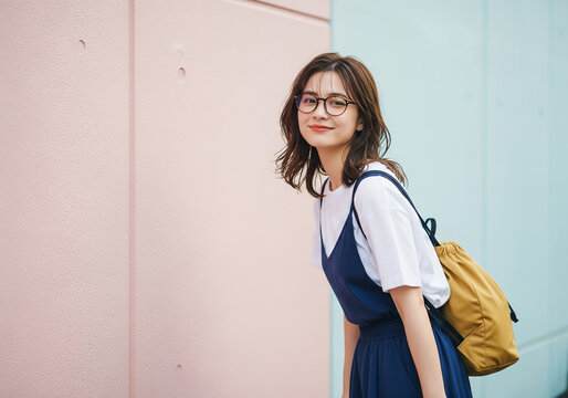 カラフルな壁の前で、キャミワンピースとリュックを合わせたメガネの日本人女性モデル