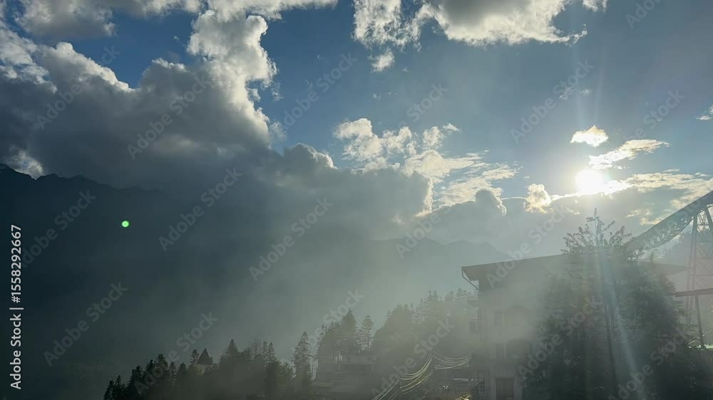 Poster sunlight rays pierce through fast-moving clouds above a misty mountain landscape. fixed shot capture