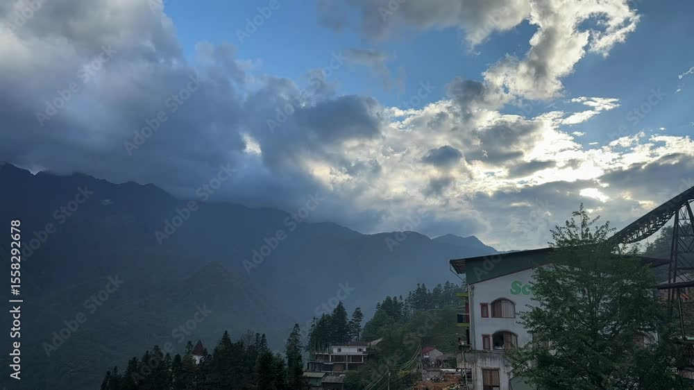 Poster clouds moving fast over misty mountains and town buildings. fixed camera captures light rays breakin