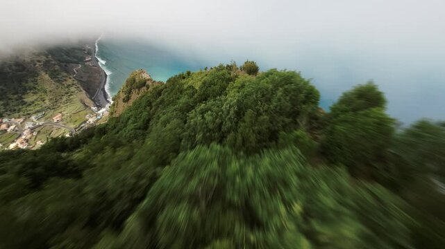 FPV drone moves above the forested cliffs of Lapas Negras in Madeira, revealing ocean views and a village below.