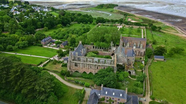 Drone pulls back from Beauport Abbey, showing the sea, beach, and surrounding gardens at Paimpol - France