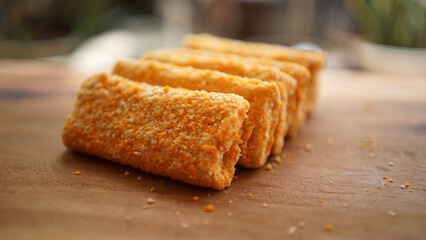Jakarta, 30 June 2025 : Frozen breaded spring rolls with kaffir lime leaves on wooden background. Raw snack food ready to cook