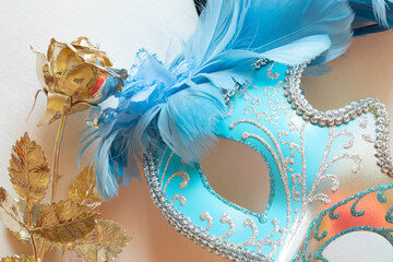 Light blue carnival mask with blue and black feathers and golden rose on white background,...