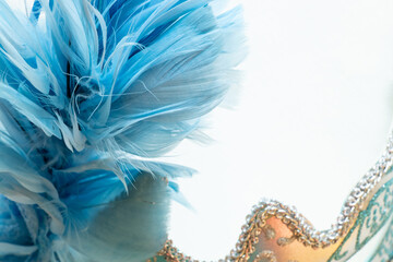Light blue carnival mask with blue and black feathers on a white background, decorative accessory