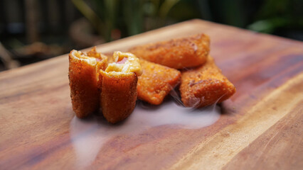 Jakarta, 30 June 2025 : Frozen breaded spring rolls with kaffir lime leaves on wooden background. Raw snack food ready to cook