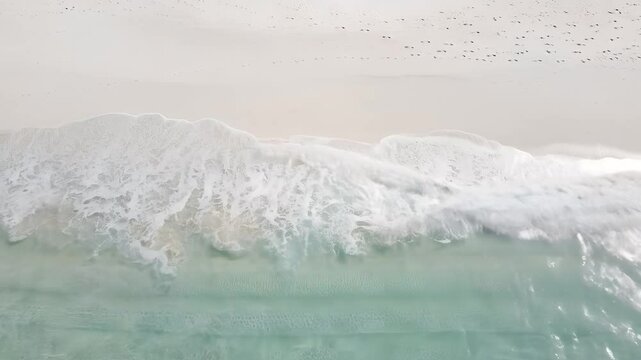 Aerial view of pristine beach wave breaking on shoreline and sandy footprints