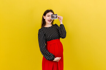 Obraz premium Cute Pregnant Lady Posing With Baby Sonography Photo Near Colored background. Concept of pregnancy, gynecology, medical test, maternal health