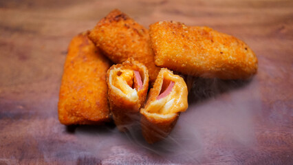 Jakarta, 30 June 2025 : Frozen breaded spring rolls with kaffir lime leaves on wooden background....
