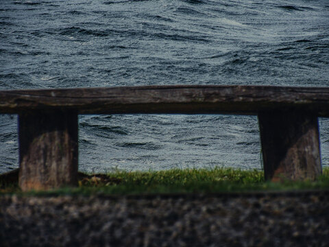 Old wooden bench facing a windy lake, with visible waves and natural textures. Peaceful, rustic scene in nature.