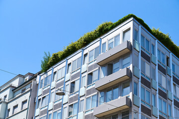A contemporary building features lush rooftop gardens against a vibrant blue sky, showcasing urban...