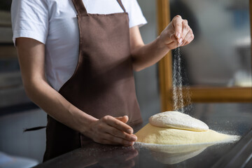 Close p of womans hands spreading flour on the dough while preparing pizza