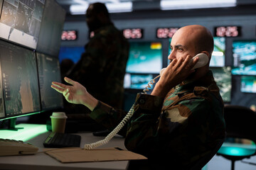 Intelligence corps specialist using communication systems to call in air strikes on enemy troops. Middle Eastern military dispatcher making phone call to request air support for ground soldiers