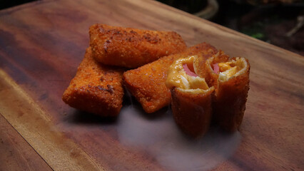 Risol mayonaise or Crispy fried breaded rolls with melted cheese and meat filling. Tasty snack served on wooden background with steam effect
