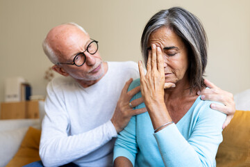 Mature man consoling depressed woman sitting on the couch at home living room. Married couple have relationship problems