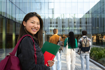 Smiling student holding books at university with friends walking away