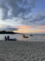 Tropical beach at sunset with dramatic clouds, colorful sky, anchored boats, and silhouettes of...